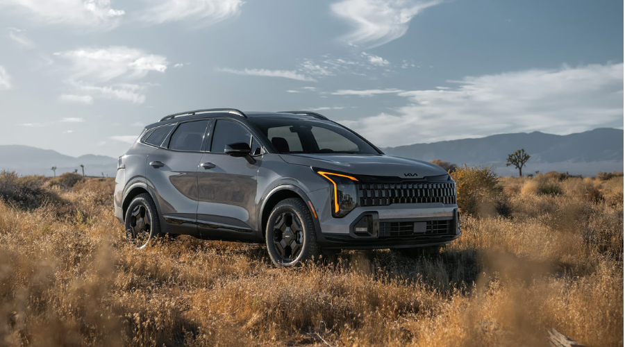 A stationary gray 2026 Kia Sportage parked in an open field, showcasing its elevated ground clearance and rugged front bumper design built for off-road performance in Waukegan and Gurnee IL.