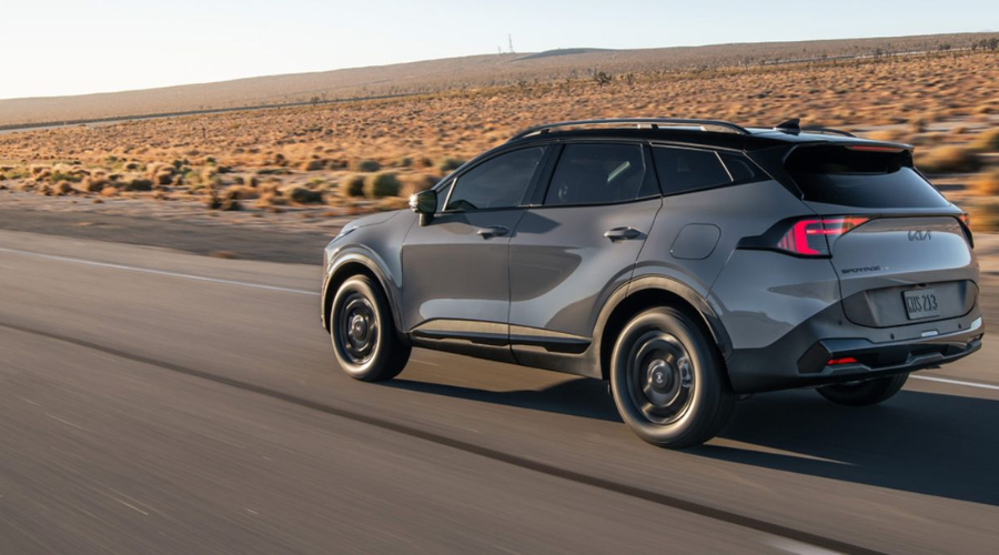 A rear-three-quarter driving shot of the gray 2026 Kia Sportage cruising on a paved highway, demonstrating smooth ride quality and stability for daily Route 41 commuters in Lake County IL.