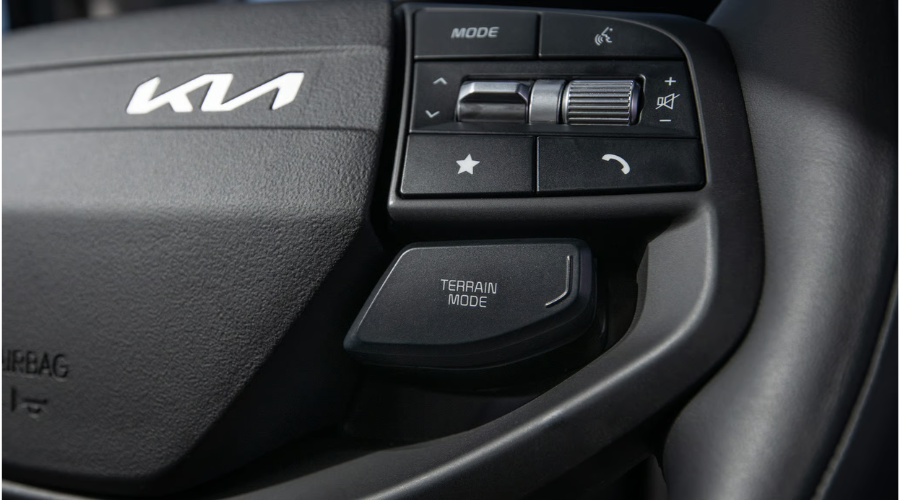 Close-up view of the 2026 Kia Sportage steering wheel controls showing the Kia emblem, customizable star shortcut button, audio toggles, and dedicated Terrain Mode switch available at Classic Kia near Waukegan, IL.