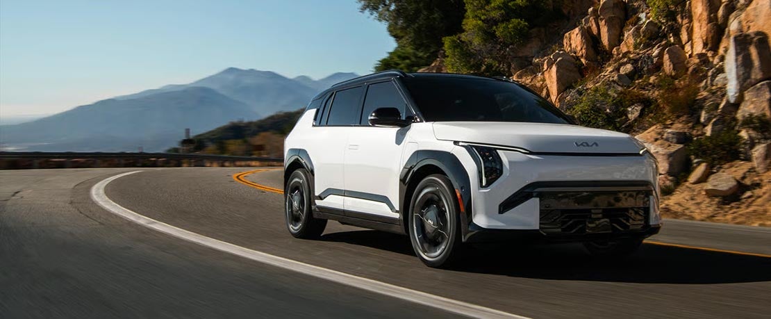 White 2027 Kia EV3 electric SUV driving on a coastal road at Classic Kia in Waukegan, IL